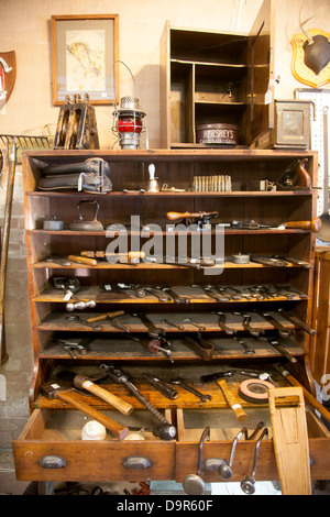 Vintage tools stored in drawers and on wooden racks.  Pictures hang on the wall. Stock Photo