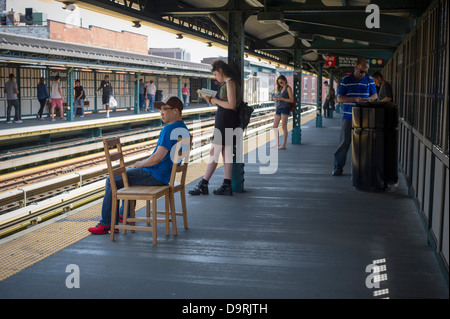 A subway commuter sits in a chair while waiting for the number seven train on a platform Stock Photo