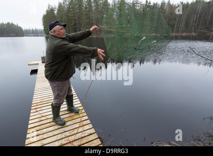 Elderly man throwing a fish trap ( katiska ) back to water , Finland Stock Photo