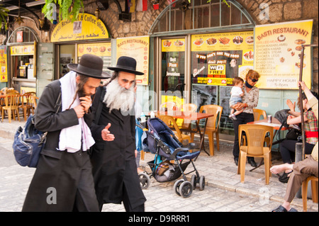 Israel Old City Jerusalem two orthodox bearded Haredi Hasidic Jewish men Jews walking past cafe coffee shop restaurant talking intensely street scene Stock Photo