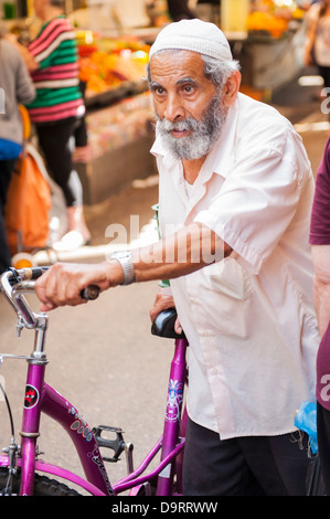 Israel Tel Aviv Jaffa Yafo Carmel Market grey gray haired bearded old man skull cap yarmulka kippah wheeling mauve pink purple bike Stock Photo