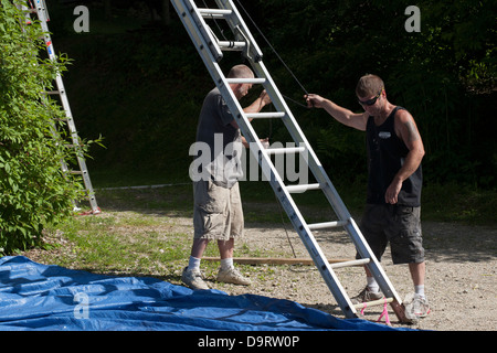 On a summer afternoon, two men clean up after a painting job. They are moving their extension ladder before they leave the job. Stock Photo