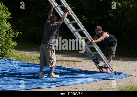 On a summer afternoon, two men clean up after a painting job. They are moving their extension ladder before they leave the job. Stock Photo