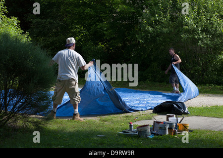 On a summer afternoon, two men clean up after a painting job.  They are folding their drop cloth before they leave the job. Stock Photo