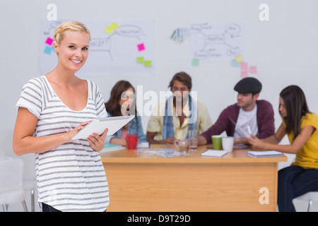 Happy editor using tablet pc as team works behind her Stock Photo