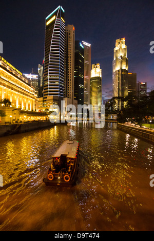the Cavenagh Bridge, a boat on the Singapore River, the Fullerton Hotel and Central Business District at night, Singapore Stock Photo