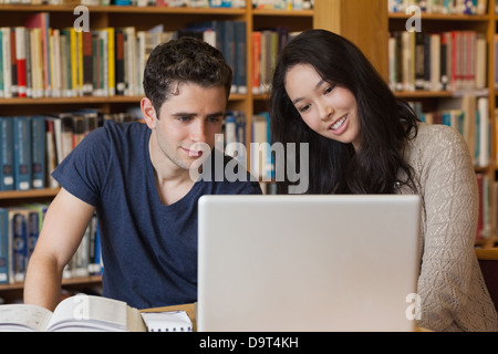 Two students learning in a library with a laptop Stock Photo