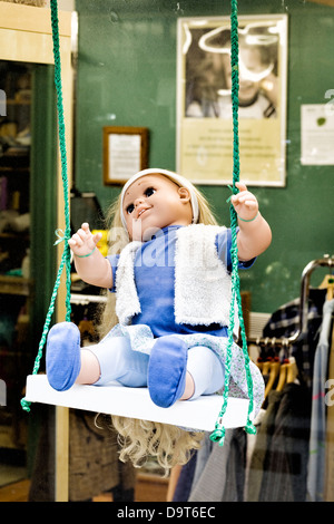 Life like Children's doll on a garden swing in a shop window Stock Photo