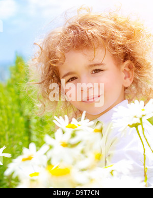 Closeup portrait of cute baby boy with beautiful curly hair on daisy field in sunny day, summer time concept Stock Photo