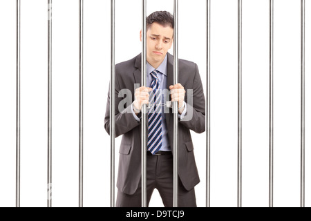 Handcuffed businessman in suit posing in jail and holding bars Stock Photo