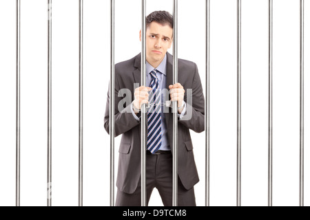 Sad handcuffed businessman in suit posing in jail and holding bars Stock Photo