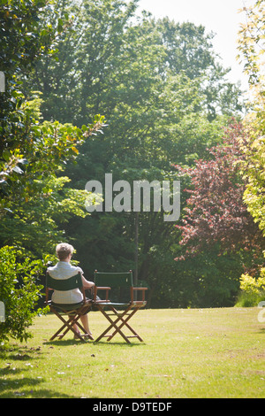 A woman sits alone reading the paper in a British park in summer Stock Photo