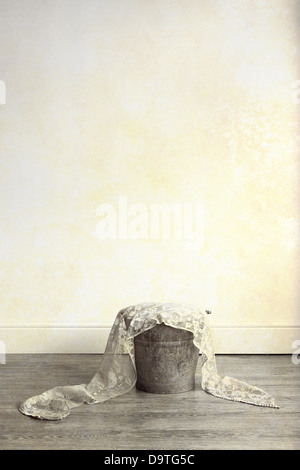 A rusty metal bucket filed with cloth, placed on a wooden floor Stock Photo