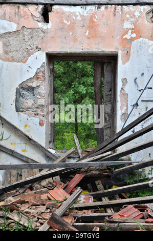 Collapsed roof chipped wall and open door with view to nature scene. Abandoned house interior. Stock Photo