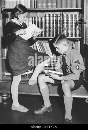 A boy in the uniform of the German Youth and a young girl are reading books in front of a book shelf in October 1938. The National Socialist propaganda from 19 October 1938 on the back of the picture: 'The book - spiritual weapon of the new time! To the first Greater German Book Week from 30 October to 6 November. Our picture shows: The young generation loves German literature, since it is only possible to connect presence with past by the good book.' Stock Photo