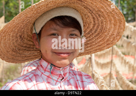 Smiling face of Burmese girl wearing straw hat in field of drying roots Myanmar (Burma) Stock Photo