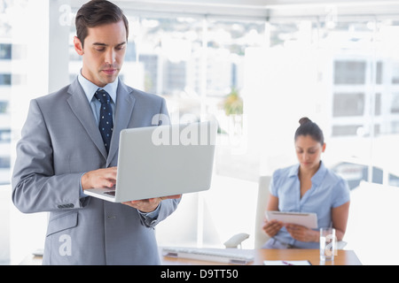 Businessman using laptop standing in office Stock Photo