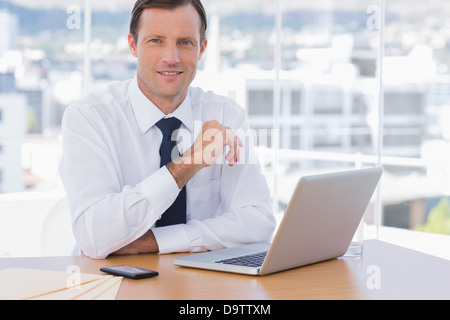 Smiling businessman leaning on his desk Stock Photo