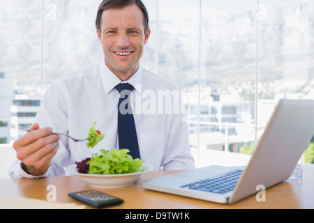 Happy businessman eating a salad on his desk Stock Photo