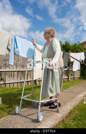 Ninety year old woman, pensioner with walking/zimmer frame checking washing on line. UK Stock Photo