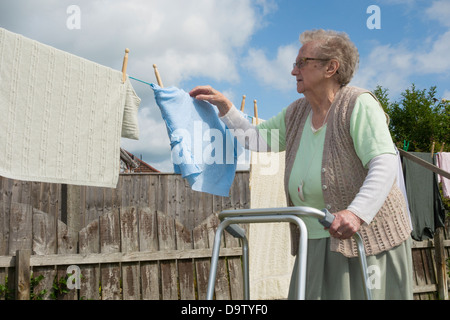 Ninety year old woman, pensioner with walking/zimmer frame checking washing on line. UK Stock Photo