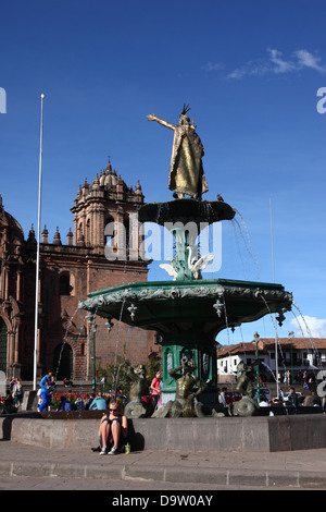 Tourist sitting next to fountain with statue of Pachacuti Inca Yupanqui or Pachacutec, cathedral in background , Cusco, Peru Stock Photo