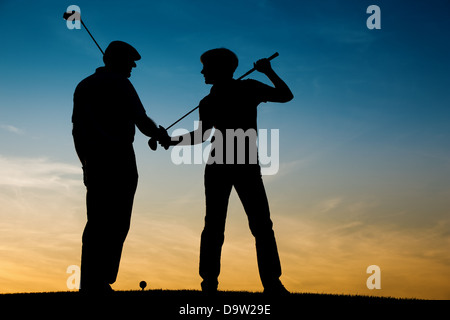 Mature or senior couple playing golf - pictured as a silhouette against an evening sky Stock Photo