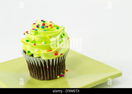 Colorful sprinkles on green frosting of chocolate cupcake on square plate with white background. Stock Photo