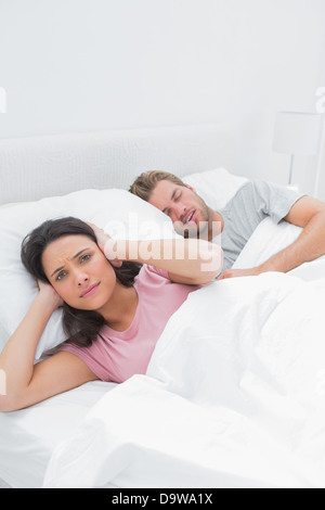 Annoyed woman covering her ears while her husband is snoring Stock Photo