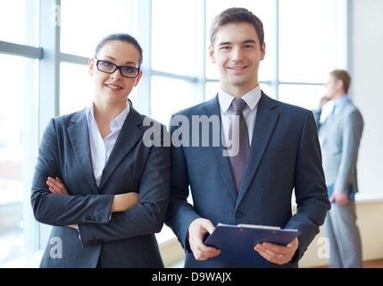 Portrait of confident business partners looking at camera with calling employee behind Stock Photo
