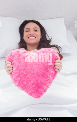 Woman lying in her bed and holding a fluffy heart cushion Stock Photo