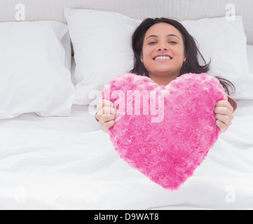 Woman in her bed holding a fluffy heart cushion Stock Photo