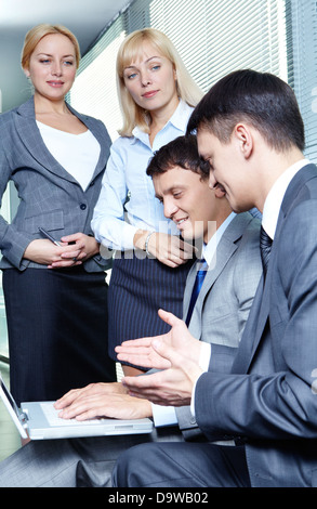 Two businessmen discussing project with pretty employees at background Stock Photo
