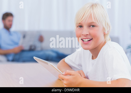 Smiling boy using tablet while his father is reading on the couch Stock Photo