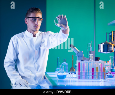 close-up of scientist sitting down near a laboratory table with chemistry glassware on top, holding a petri dish analysing it Stock Photo