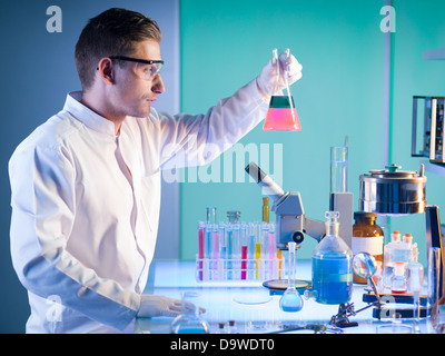 side view of male scientist in a chemistry laboratory holding a flask with colorful fluid, making a discovery Stock Photo