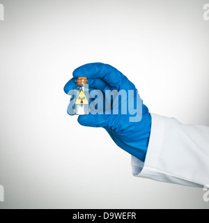white background with hand in blue glove and white lab coat holding a small transparent bottle labeled as radioactive with a transparent colorless liquid Stock Photo