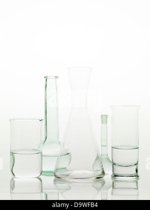 frontal view of different types of glass containers used in the laboratory, filled with transparent colorless liquid and one empty, with a white background Stock Photo