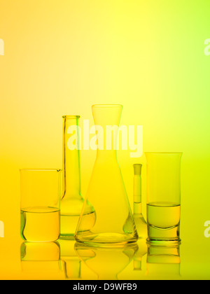 frontal view of different types of glass containers used in the laboratory, filled with transparent colorless liquid and one empty, with a bright yellow background Stock Photo