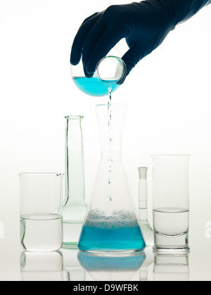 frontal view of different types of glass containers used in the laboratory, filled with transparent colorless liquid and one in which someone is pouring a blue liquid Stock Photo