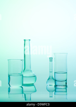 frontal view of different types of glass containers used in the laboratory, filled with transparent colorless liquid and one empty, with a gradient blue background Stock Photo