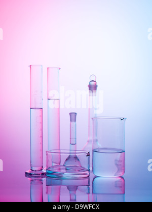 frontal view of different types of glass containers used in the laboratory, filled with transparent colorless liquid and one empty, with a gradient purple, blue and white background Stock Photo