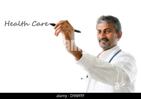 Health care concept. Mature Indian male medical doctor writing on blank space, standing isolated on white background. Handsome Indian model portrait. Stock Photo