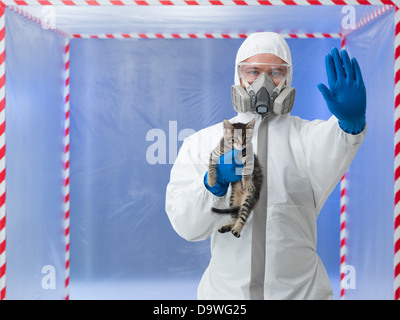 close-up of male scientist wearing protection equipment, holding little cat, with stop gesture, in chamber surounded with red and white tape Stock Photo