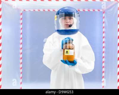 Person in a biohazard suit with a toxic substance in a brown bottle labelled as a poison held in her hands Stock Photo