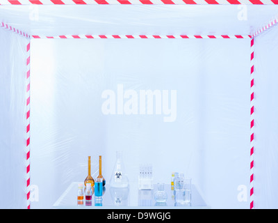 different glass containers filled with differently colored liquids on a glass table in a containment tent, lit by a white light Stock Photo