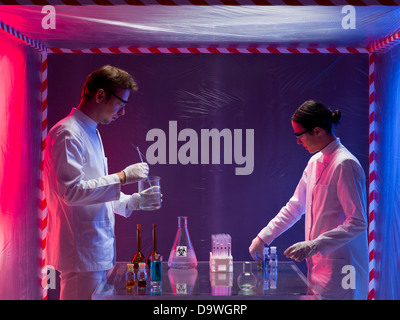 two scientists, a man and a woman, working with chemicals in a containment tent, lit by a gradient red and blue light Stock Photo