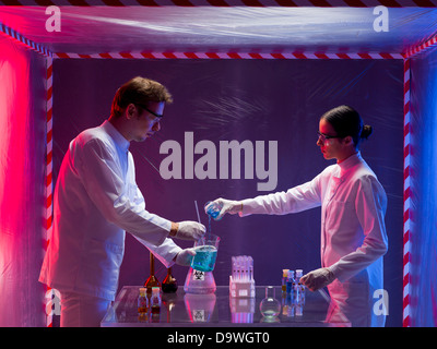 two scientists, a man and a woman, working with chemicals in a containment tent, lit by a gradient red and blue light Stock Photo