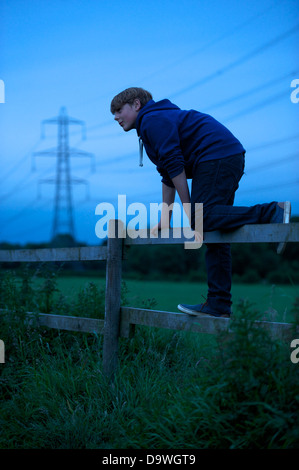 A young boys climbs a fence with electric power lines in the background Stock Photo
