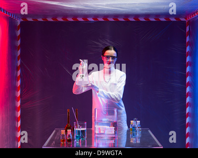 woman scientist wearing a white lab coat and protection goggles holding a bottle labeled as bio hazardous with both hands in fro Stock Photo